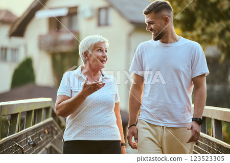 A handsome man and an older woman share a serene walk in nature, crossing a beautiful bridge against the backdrop of a stunning sunset, embodying the concept of a healthy and vibrant intergenerational A handsome man and an older woman share a serene walk in nature, crossing a beautiful bridge against the backdrop of a stunning sunset, embodying the concept of a healthy and vibrant intergenerational 123523305