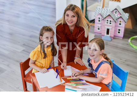 Creative kids during an art class in a daycare center or elementary school classroom drawing with female teacher. 123523412