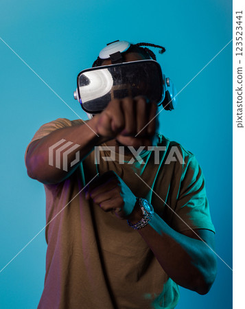In an avant-garde scene, an African American man engages in cutting-edge virtual reality gaming, utilizing VR glasses to immerse himself in futuristic boxing games, set against a vivid blue background In an avant-garde scene, an African American man engages in cutting-edge virtual reality gaming, utilizing VR glasses to immerse himself in futuristic boxing games, set against a vivid blue background 123523441