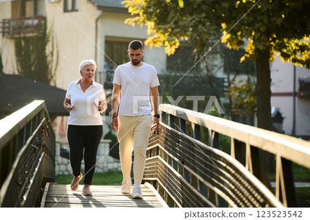 A handsome man and an older woman share a serene walk in nature, crossing a beautiful bridge against the backdrop of a stunning sunset, embodying the concept of a healthy and vibrant intergenerational A handsome man and an older woman share a serene walk in nature, crossing a beautiful bridge against the backdrop of a stunning sunset, embodying the concept of a healthy and vibrant intergenerational 123523542