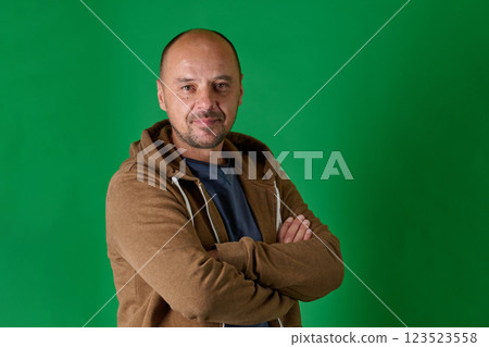 Middle aged bald man in casual attire with crossed arms poses confidently against a green studio backdrop. Middle aged bald man in casual attire with crossed arms poses confidently against a green studio backdrop. 123523558