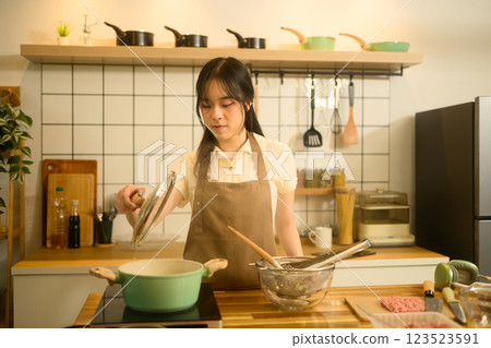 Asian woman cooking spaghetti in her kitchen adding ingredients to a pot on the stove Asian woman cooking spaghetti in her kitchen adding ingredients to a pot on the stove 123523591