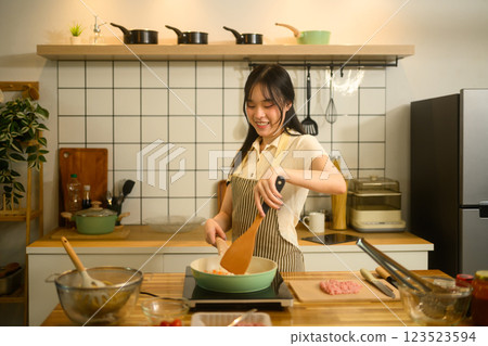 Young woman stirring ingredients in in a pan, preparing spaghetti in her cozy kitchen Young woman stirring ingredients in in a pan, preparing spaghetti in her cozy kitchen 123523594