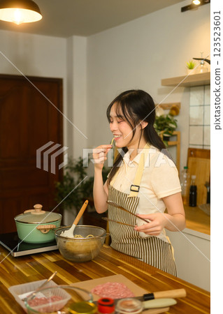 Young Asian woman checking the doneness of her spaghetti in cozy kitchen 123523601