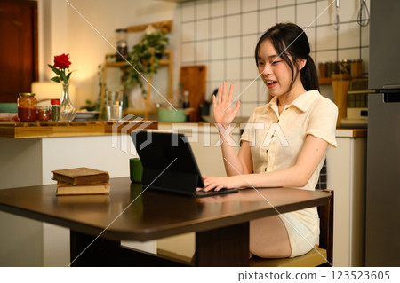 Cheerful woman sitting at a kitchen table, participating in a video call on digital tablet 123523605