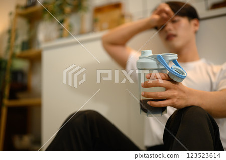 Tired man resting on the floor, drinking a protein shake after a workout 123523614