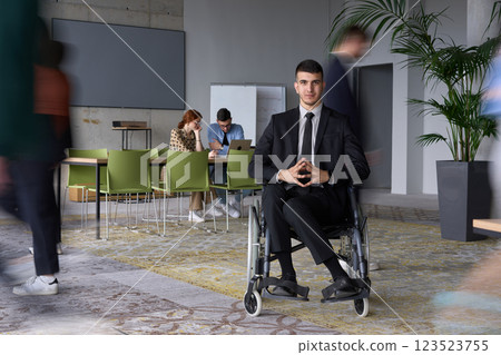 A businessman in a wheelchair navigating through a busy office, surrounded by his colleagues who are actively engaged in their work and collaboration A businessman in a wheelchair navigating through a busy office, surrounded by his colleagues who are actively engaged in their work and collaboration 123523755