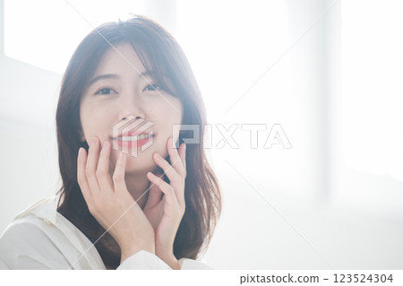 A young woman in her 20s wearing a white backlit room, making use of makeup and beauty products A young woman in her 20s wearing a white backlit room, making use of makeup and beauty products 123524304