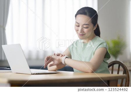 一位 30 多歲的女性在辦公桌前工作時正在看智慧手錶 123524492