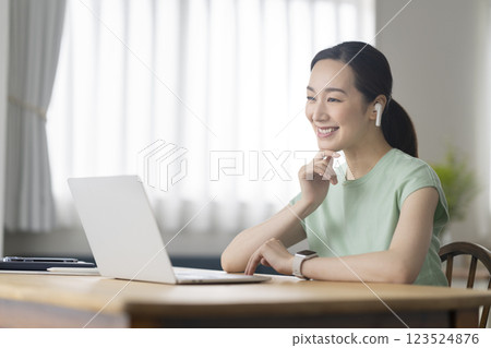 A woman in her 30s wearing earphones and facing a laptop computer, telework, online call image 123524876