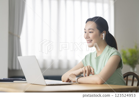 一位 30 多歲女性戴著耳機，面對著筆記型電腦，遠端辦公，線上通話圖片 123524953