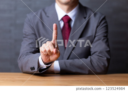A middle-aged male businessman wearing a gray suit and pointing his index finger 123524984