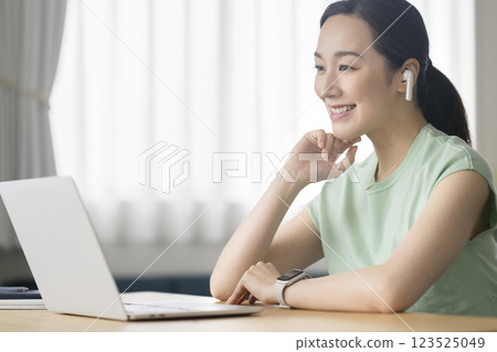 A woman in her 30s wearing earphones and facing a laptop computer, telework, online call image 123525049