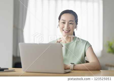 一位 30 多歲女性戴著耳機，面對著筆記型電腦，遠端辦公，線上通話圖片 123525051