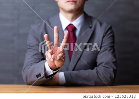 A middle-aged male businessman wearing a gray suit and pointing up three fingers A middle-aged male businessman wearing a gray suit and pointing up three fingers 123525318