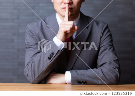 一位身穿灰色西裝、用手指摀住嘴巴的中年男性商人 123525319