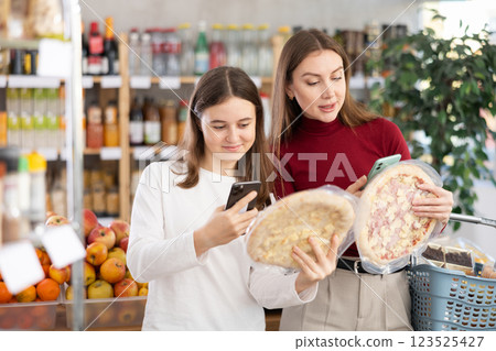 Teenage girl and her mother scanning QR on pizza in supermarket Teenage girl and her mother scanning QR on pizza in supermarket 123525427