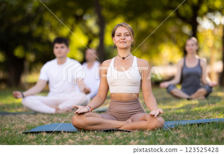 Girl meditating in lotus position during group yoga in park 123525428