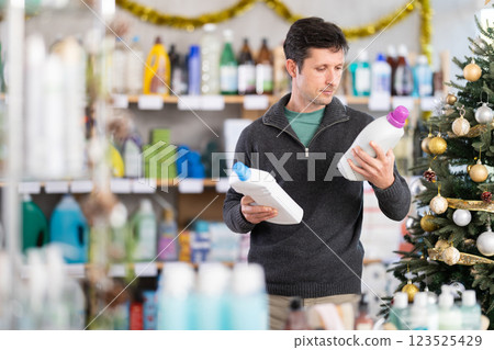 Adult man buyer chooses detergent in decorated household chemicals store 123525429