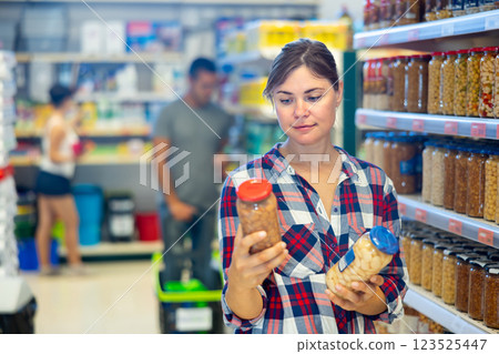 Young woman choosing canned beans in sauce in supermarket 123525447