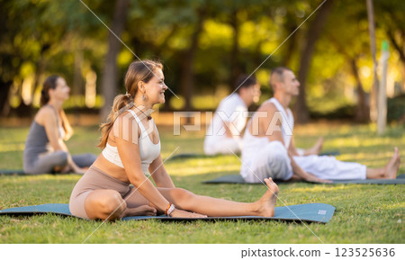 Yoga lesson visitors with coach perform Parivritta Janu Shirshasana in park Yoga lesson visitors with coach perform Parivritta Janu Shirshasana in park 123525636