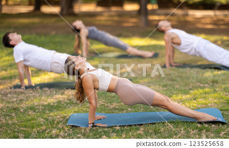 Girl holding Upward Plank Pose during group yoga in park Girl holding Upward Plank Pose during group yoga in park 123525658