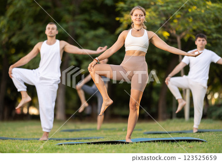 Yoga lesson visitors with coach perform Parivritta Hasta Padangushthasana in park 123525659