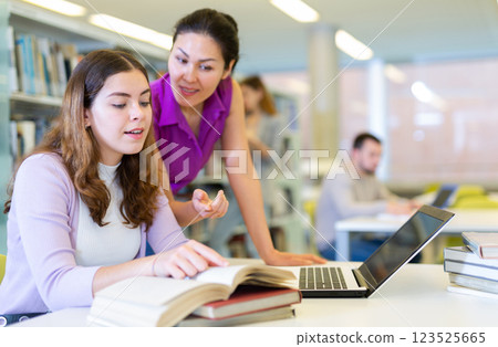 Two female scientists using books and laptop for research in library 123525665