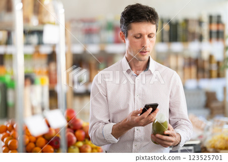 Man in light shirt scan QR code and take reading green smoothie label using phone camera in shop Man in light shirt scan QR code and take reading green smoothie label using phone camera in shop 123525701