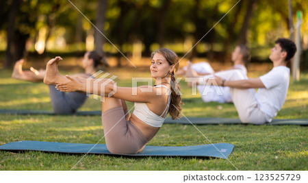 Yoga lesson visitors perform Paripurna Navasana in park 123525729