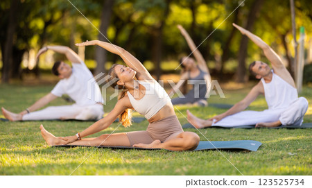 Yoga lesson visitors with coach perform Parivritta Janu Shirshasana in park 123525734