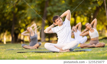 Guy stretching in lotus position during group yoga in park 123525877