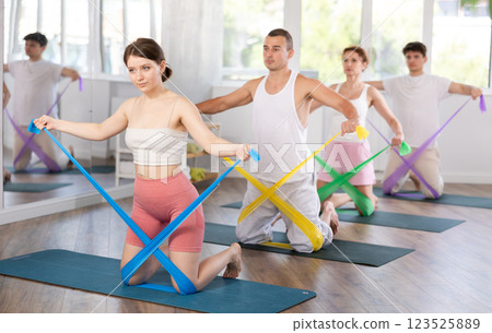 Young men and women doing arm workout with resistance band standing on knees 123525889