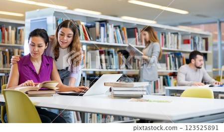 Caring woman helping friend to prepare for exams in library Caring woman helping friend to prepare for exams in library 123525891