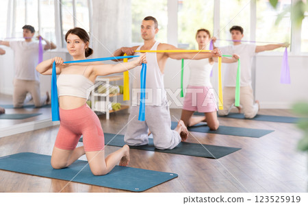 Young men and women doing arm workout with resistance band standing on knees 123525919