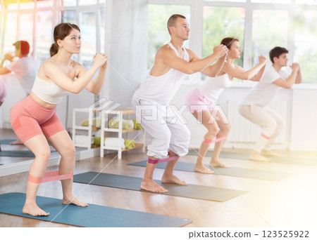 Group of women and men standing and doing stretching exercise with resistance bands in fitness studio Group of women and men standing and doing stretching exercise with resistance bands in fitness studio 123525922