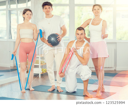 Young men and women posing together in training room holding resistance bands and pilates ball Young men and women posing together in training room holding resistance bands and pilates ball 123525994