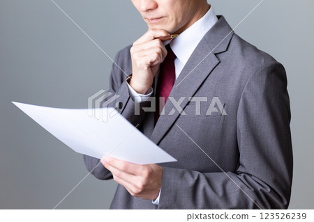 A middle-aged male businessman wearing a gray suit looking at documents 123526239