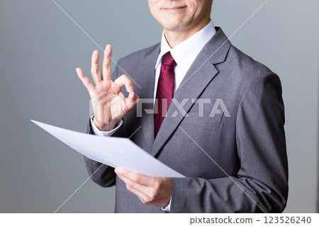 A middle-aged male businessman wearing a gray suit and holding a document making a circle sign 123526240