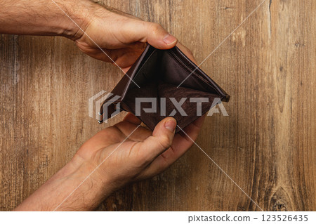 Man holds empty wallet while facing financial crisis and uncertainty Man holds empty wallet while facing financial crisis and uncertainty 123526435