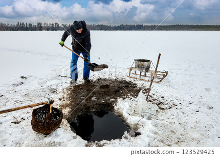 Farmer extracts sapropel sludge from freshwater lake through ice hole, he loads muck into container, using sled to haul organic fertilizer for agriculture. Farmer extracts sapropel sludge from freshwater lake through ice hole, he loads muck into container, using sled to haul organic fertilizer for agriculture. 123529425