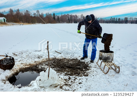 Farmer mines sapropel freshwater sediments by pulling basket of lake muck through ice, he then transports nutrient-rich goop on sled for agriculture. 123529427