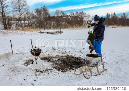 From lake bottom, man extracts humic substances sapropel, basket gathers water sediment, transfers it to container, and sled moves it for soil improving. 123529428