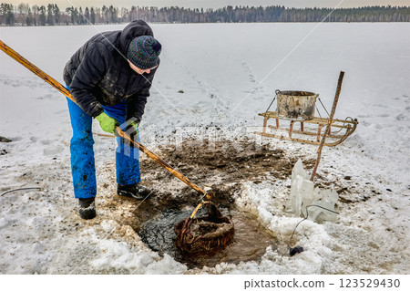 Farmer extracting sapropel from a freshwater lake through an ice hole, using a basket and sled, for use as organic fertilizer. Farmer extracting sapropel from a freshwater lake through an ice hole, using a basket and sled, for use as organic fertilizer. 123529430
