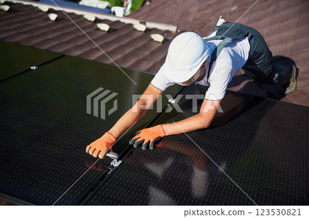 Worker building photovoltaic solar panel system on rooftop of house. Man engineer in helmets and gloves installing solar module with help of hex key outdoors. Renewable energy generation concept. 123530821