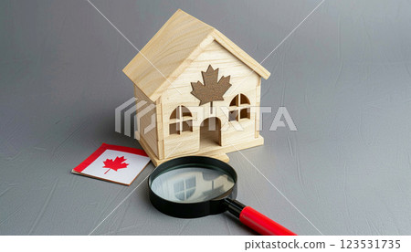 A wooden house model and magnifying glass on a Canada flag against a gray background, symbolizing real estate search in Canada 123531735