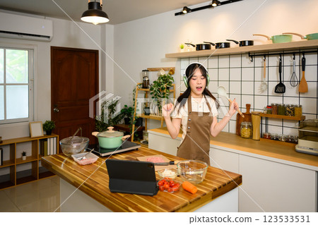 Joyful young woman listening to music through headphones and dancing in the kitchen Joyful young woman listening to music through headphones and dancing in the kitchen 123533531
