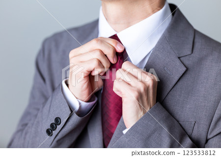 A middle-aged male businessman wearing a gray suit and fixing his tie 123533812
