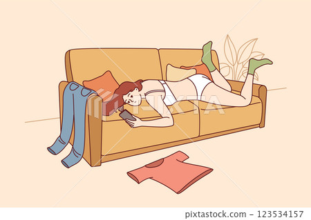 Lazy woman in underwear lies on sofa and uses phone, not paying attention to chaos in apartment 123534157