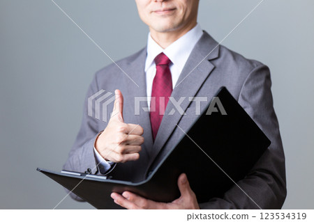 Middle-aged male businessman holding documents and giving thumbs up 123534319